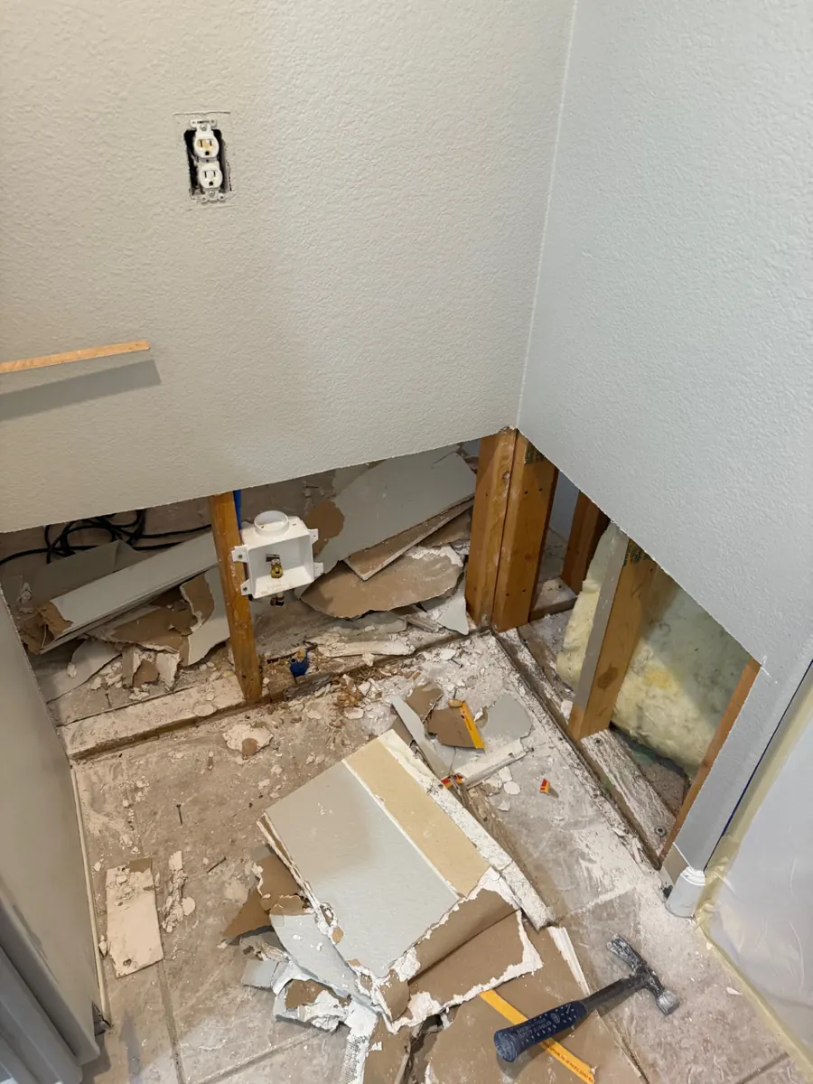 Before: laundry wall with lower drywall cut out around the washer box in Anthem