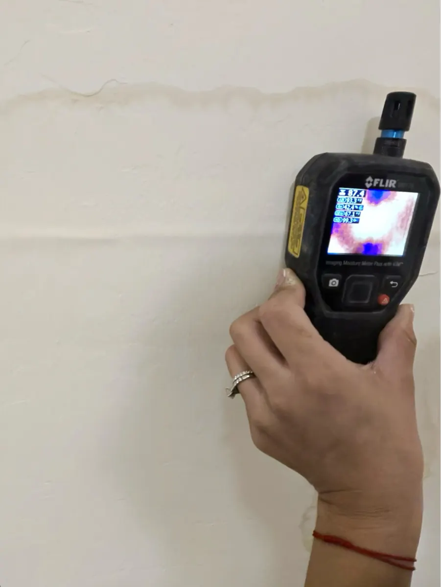 Moisture meter held against a stained closet wall in a Cadence home