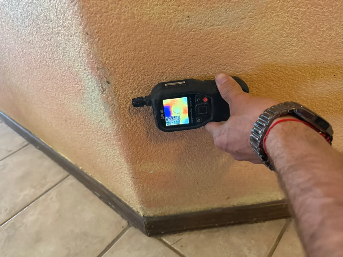 Thermal moisture meter held against a hallway wall above the baseboard in a Centennial Hills home