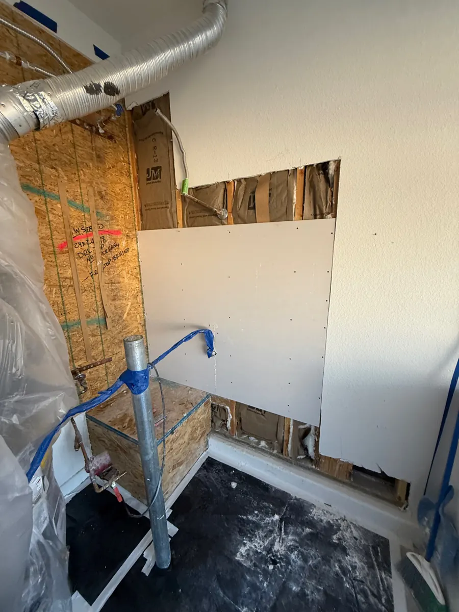 New drywall repair screwed into an opened wall beside a water heater stand in a Centennial Hills home