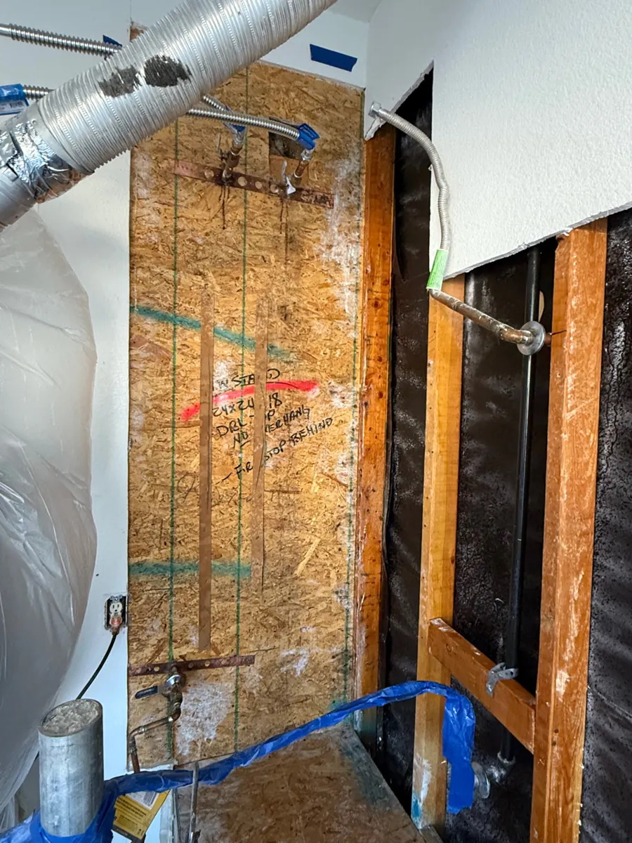 Before: wall behind a water heater stand opened to framing and sheathing in a Centennial Hills home