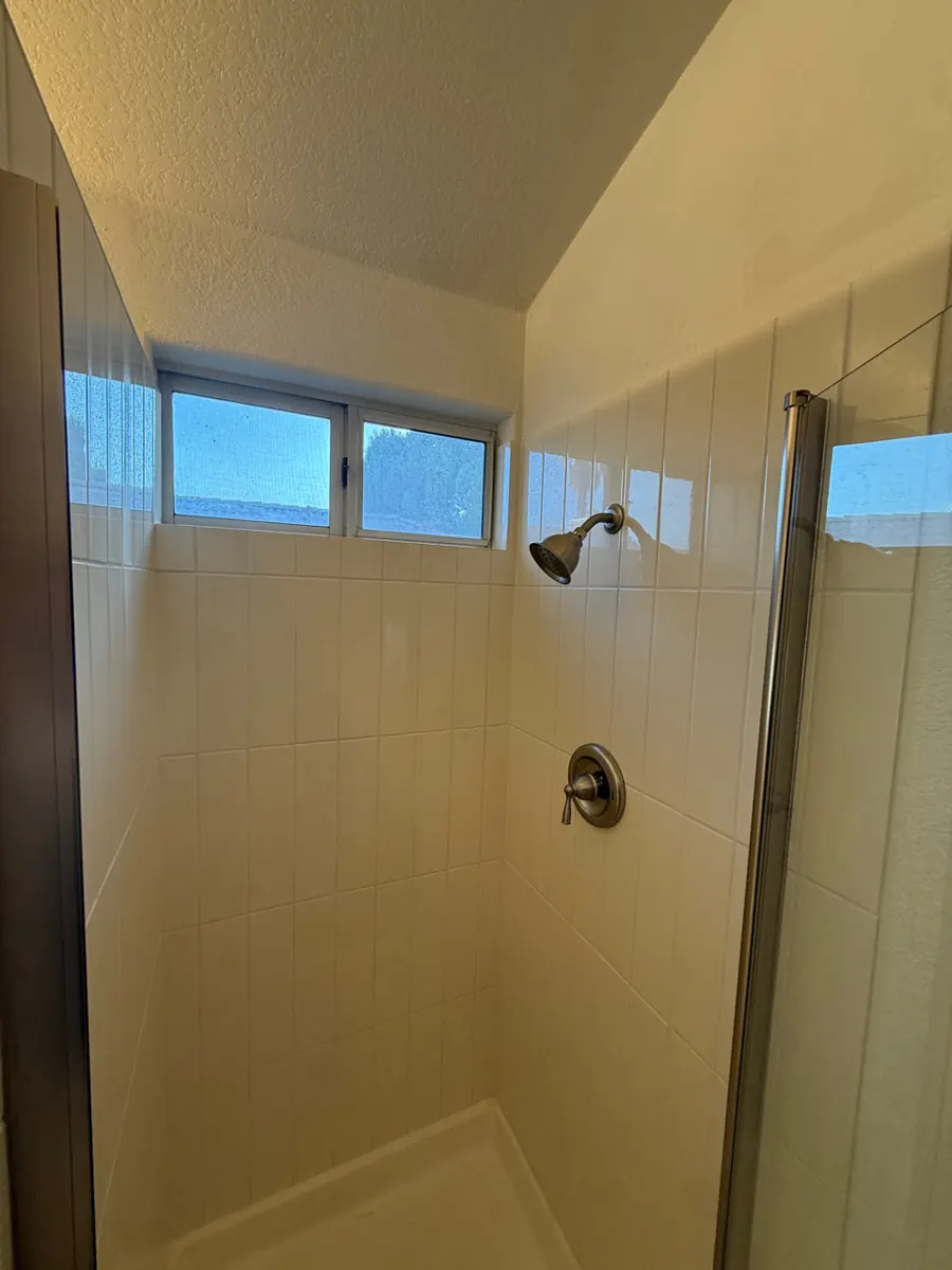 After: rebuilt shower with new white tile, glass door and window in a Desert Shores bathroom
