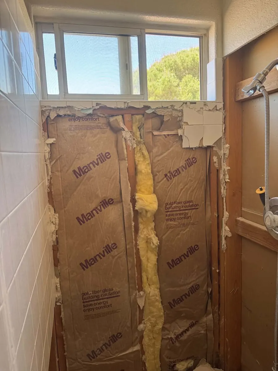 Before: shower wall under a window opened to insulation and studs in a Desert Shores home
