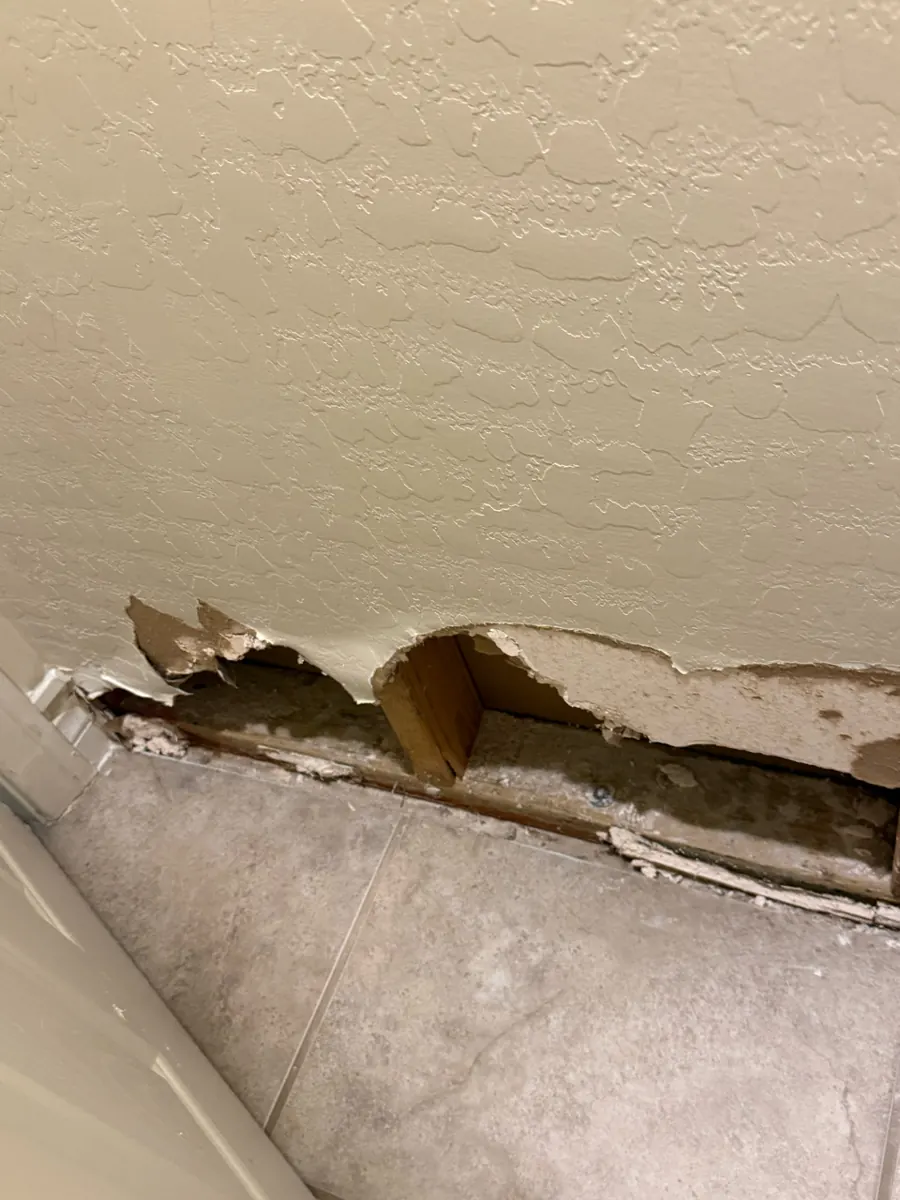 Broken, wet drywall at the base of a bathroom wall in an Enterprise home