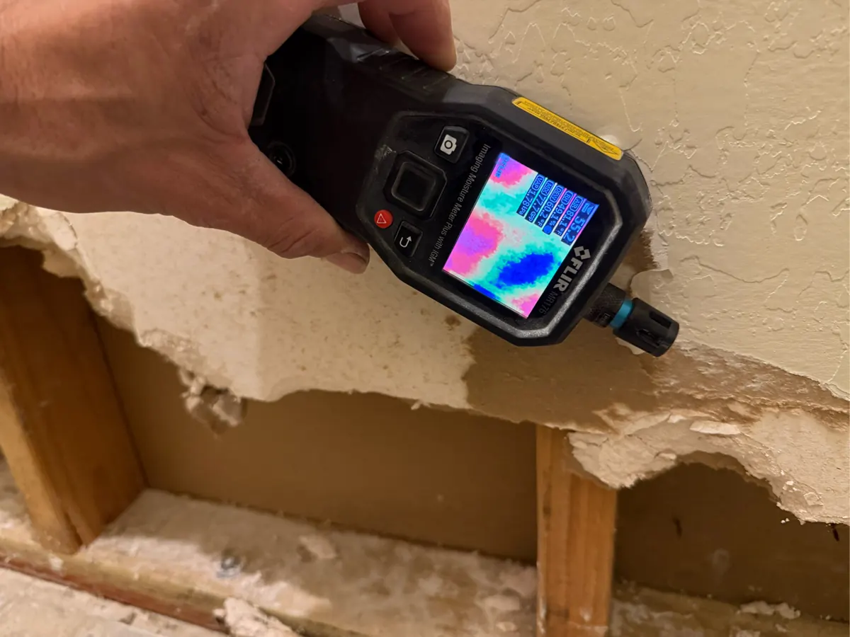 Imaging moisture meter held on a bathroom wall above opened drywall in Enterprise