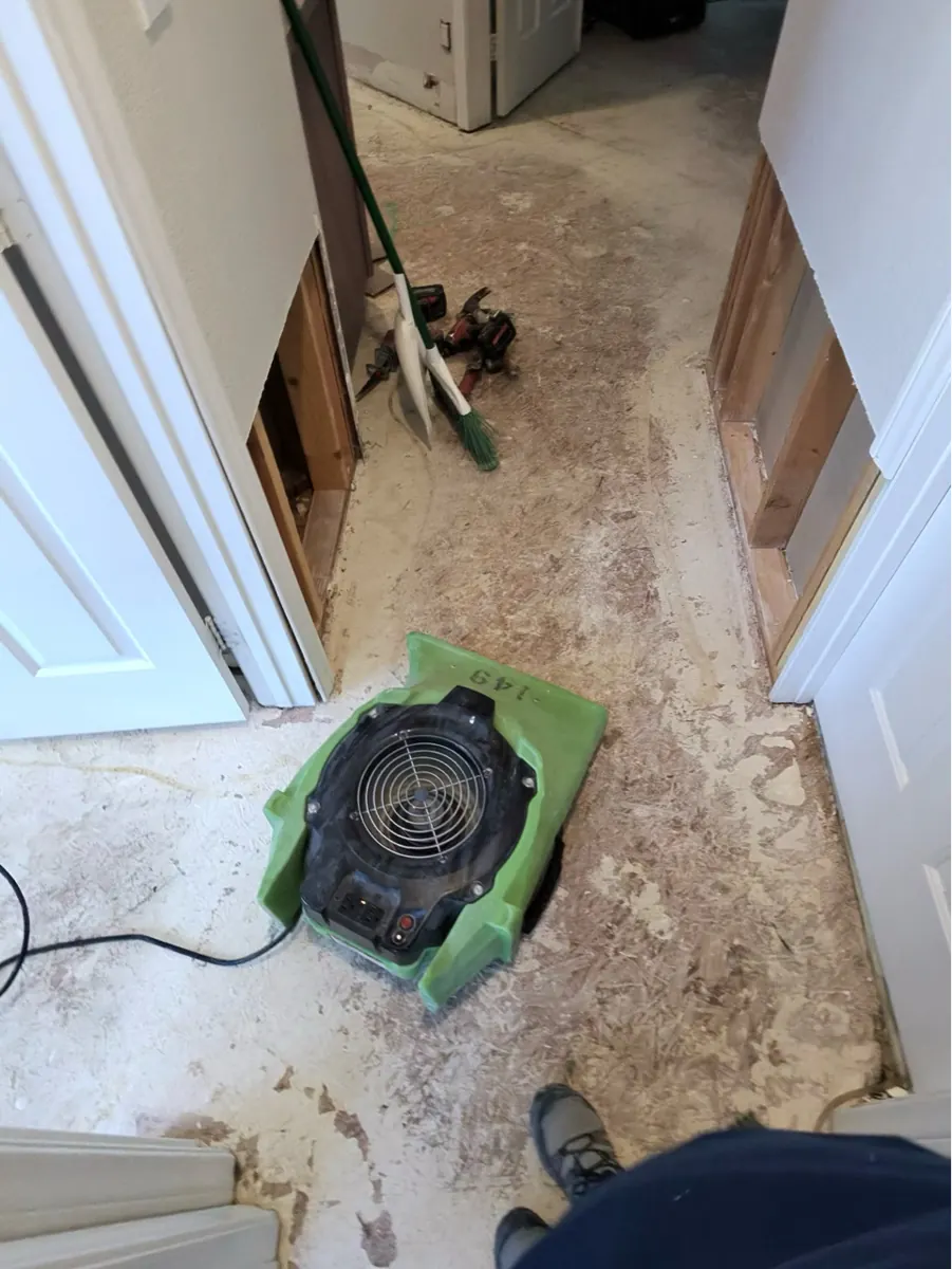 Before: hallway with flooring and lower drywall removed and an air mover in Green Valley North