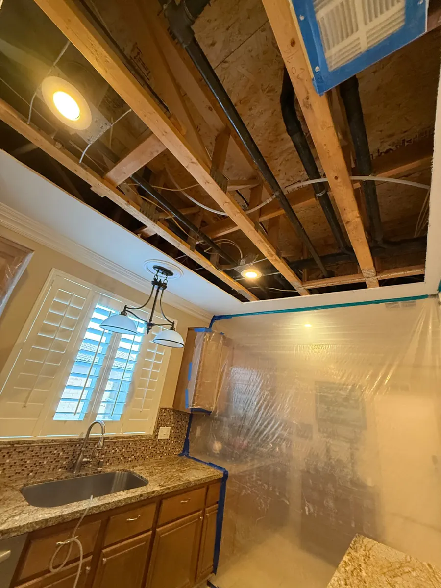Kitchen ceiling opened to the joists and plumbing above a sink in a Lone Mountain home
