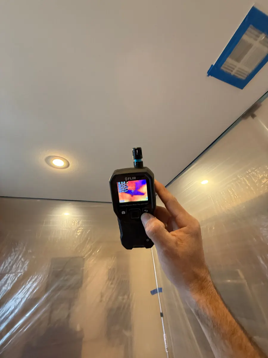 Thermal moisture meter held up to a kitchen ceiling inside plastic containment in a Lone Mountain home