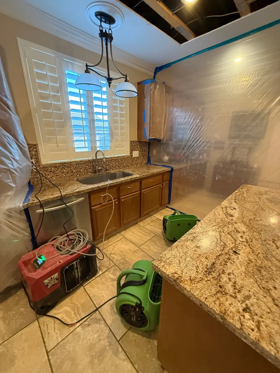 Dehumidifier and air movers on a tile kitchen floor inside containment in a Lone Mountain home