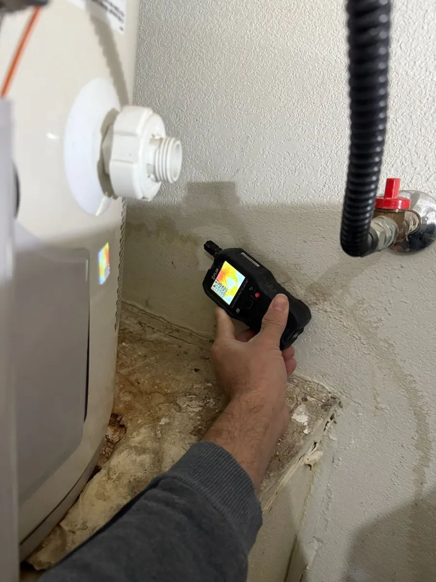 Thermal moisture meter at the stained wall base beside a water heater in a Lone Mountain garage