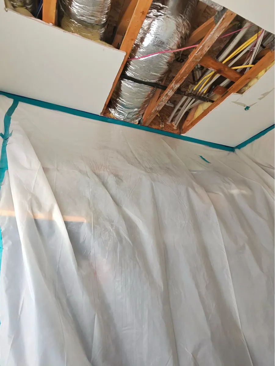 Ceiling drywall removed over ductwork inside plastic containment in a Paradise Hills home