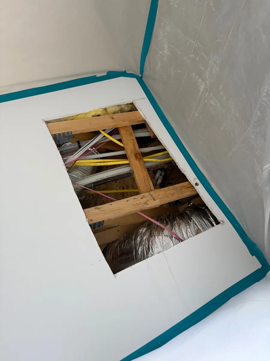 Square opening cut in a ceiling showing joists and water lines in a Paradise Hills home