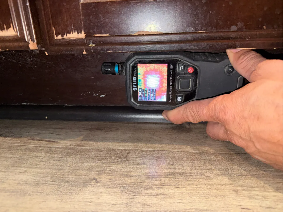 Thermal moisture meter held against a kitchen cabinet toe kick in a Providence home