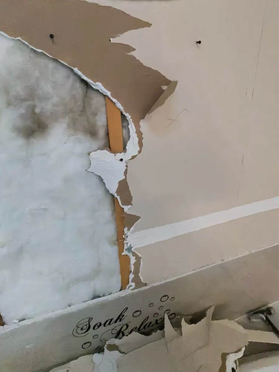 Drywall torn away above a tub to expose insulation in a River Mountain bathroom