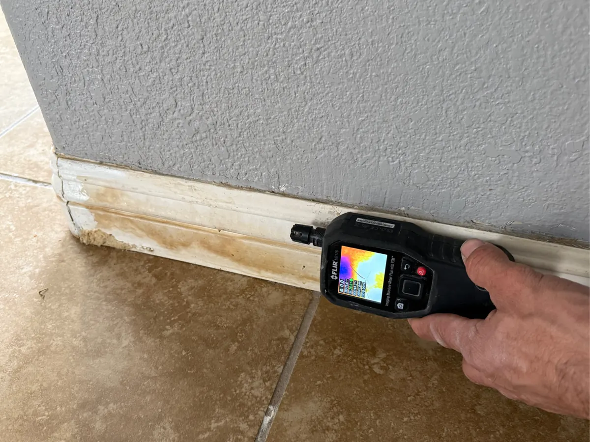 Moisture meter on a stained baseboard along a tile floor in a Silverado Ranch home