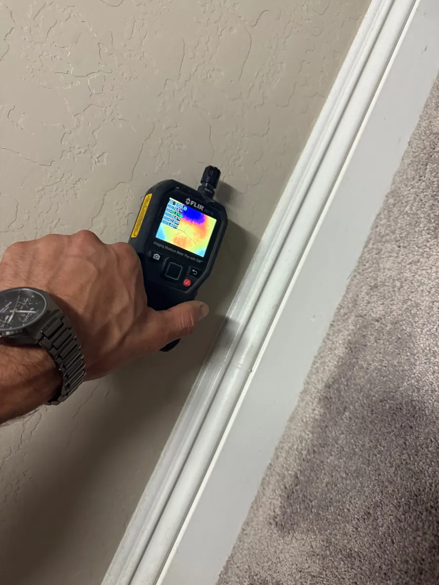 Thermal moisture meter held at a closet baseboard above carpet in a Skye Canyon home