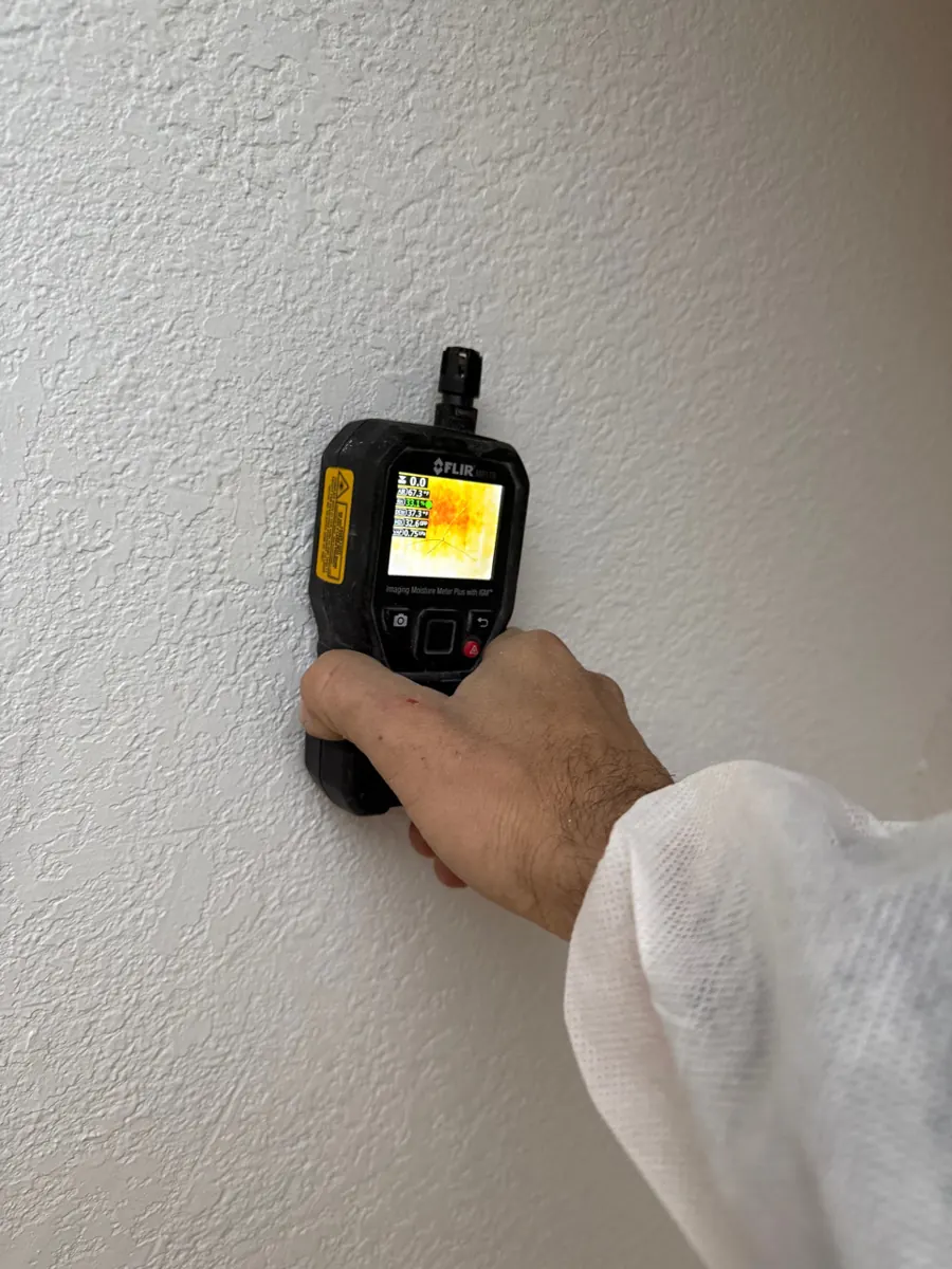 Thermal moisture meter held to a textured wall by a technician in a protective suit in Southern Highlands