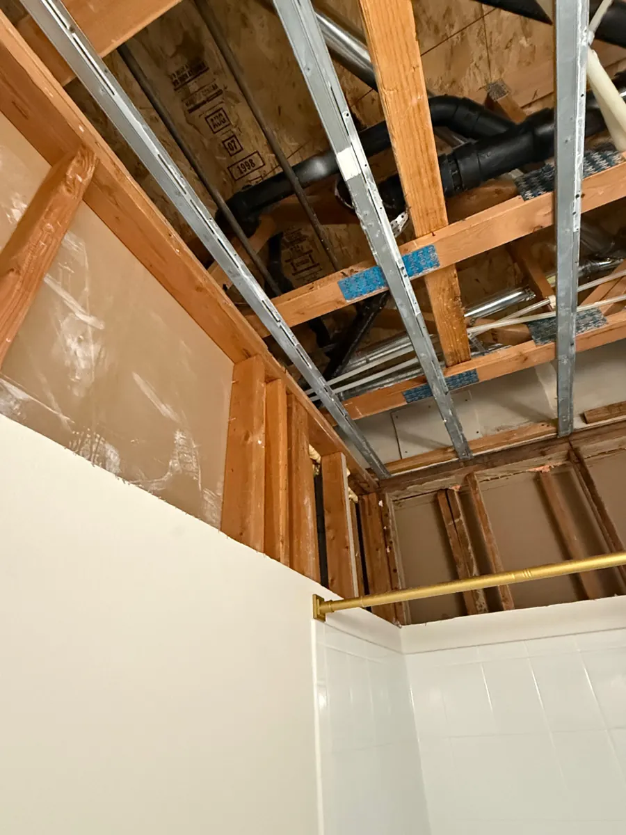 Bathroom ceiling opened to joists, drain lines and framing above a tub in Spring Valley