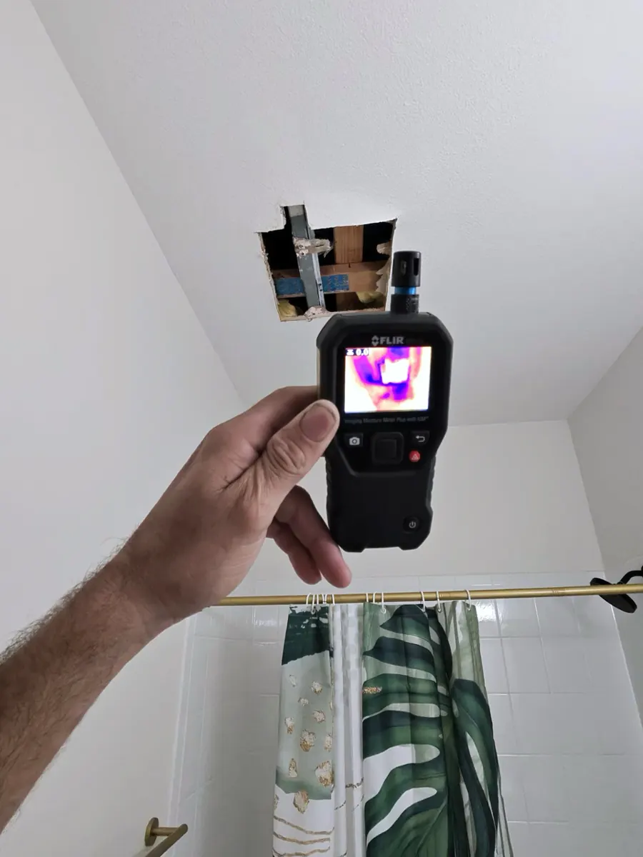 Thermal moisture meter held up to a bathroom ceiling above a tub in a Spring Valley home