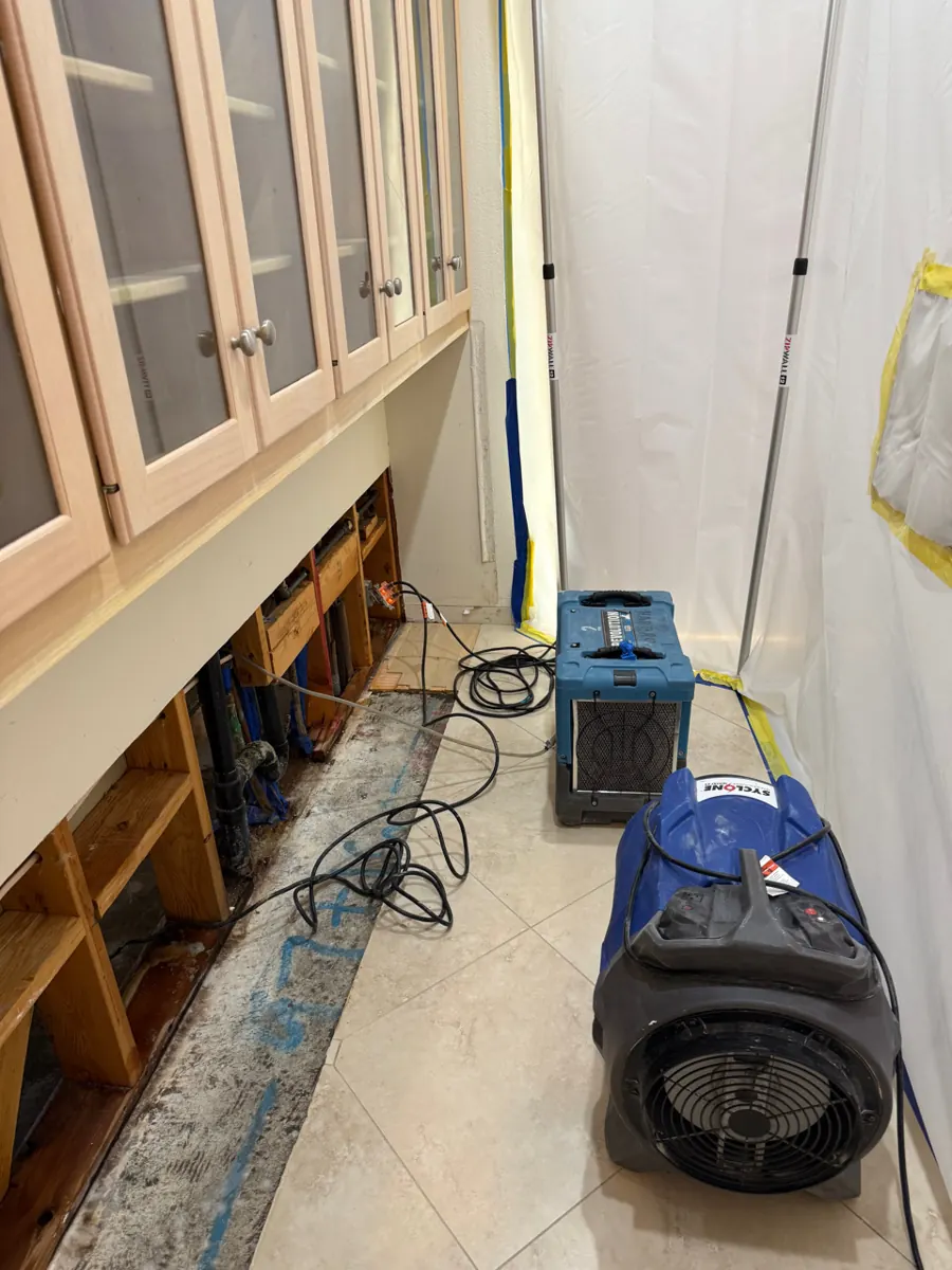 Air mover and dehumidifier inside containment beside opened cabinets in a Spring Valley home