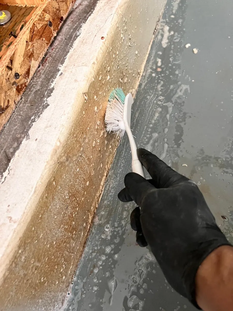 Gloved hand scrubbing a concrete garage curb with a brush in a Spring Valley condo