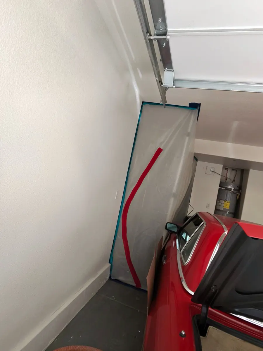 Plastic containment with a red zipper door set up beside a parked car in a Spring Valley condo garage