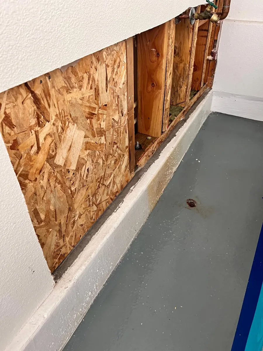 Garage wall opened to sheathing and studs above a concrete curb in a Spring Valley condo