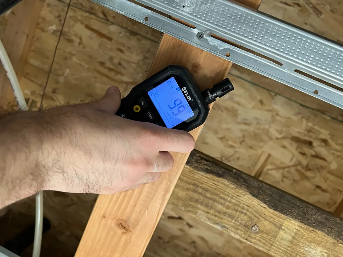 Moisture meter pressed against an exposed ceiling joist in a Spring Valley bathroom