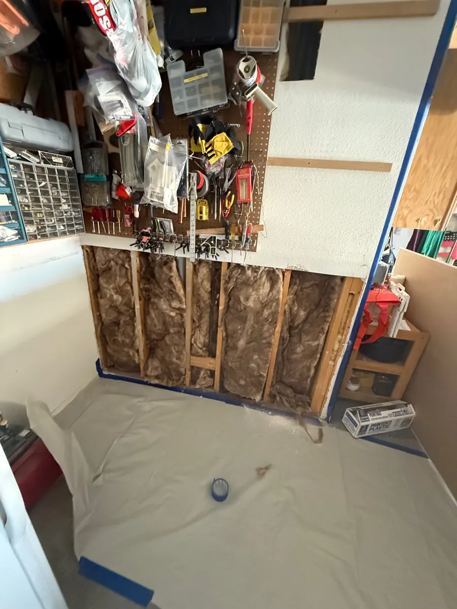 Lower garage wall opened to insulation and studs above a paper-covered floor in Sun City Summerlin