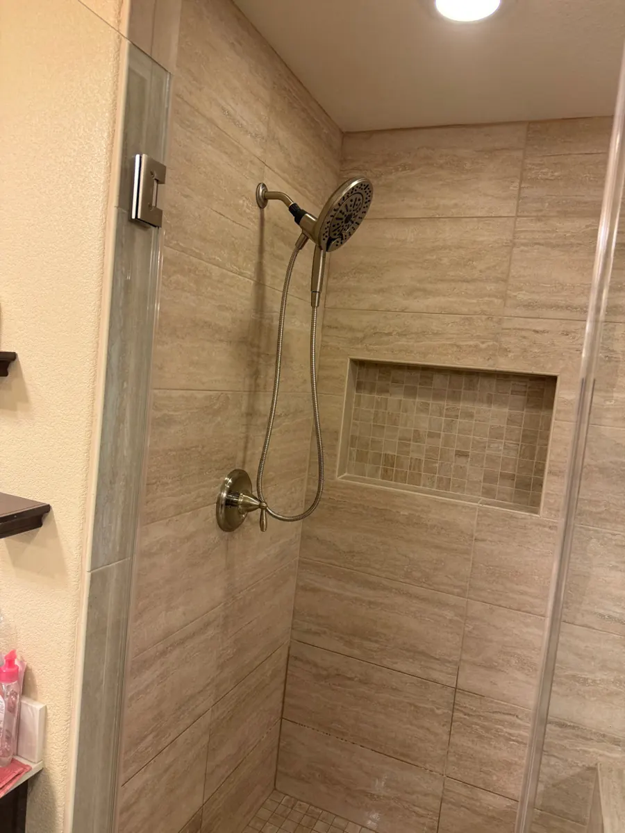 Finished tiled shower with glass door, niche and handheld head in a West Henderson home