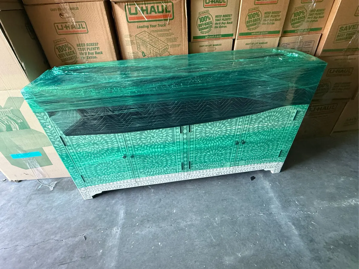 Cabinet wrapped in plastic beside stacked boxes in storage for a Whitney pack-out