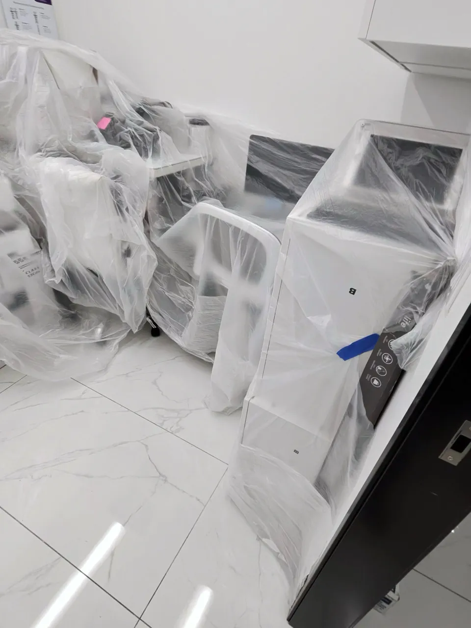 Furniture and equipment wrapped in clear plastic inside a tiled commercial room