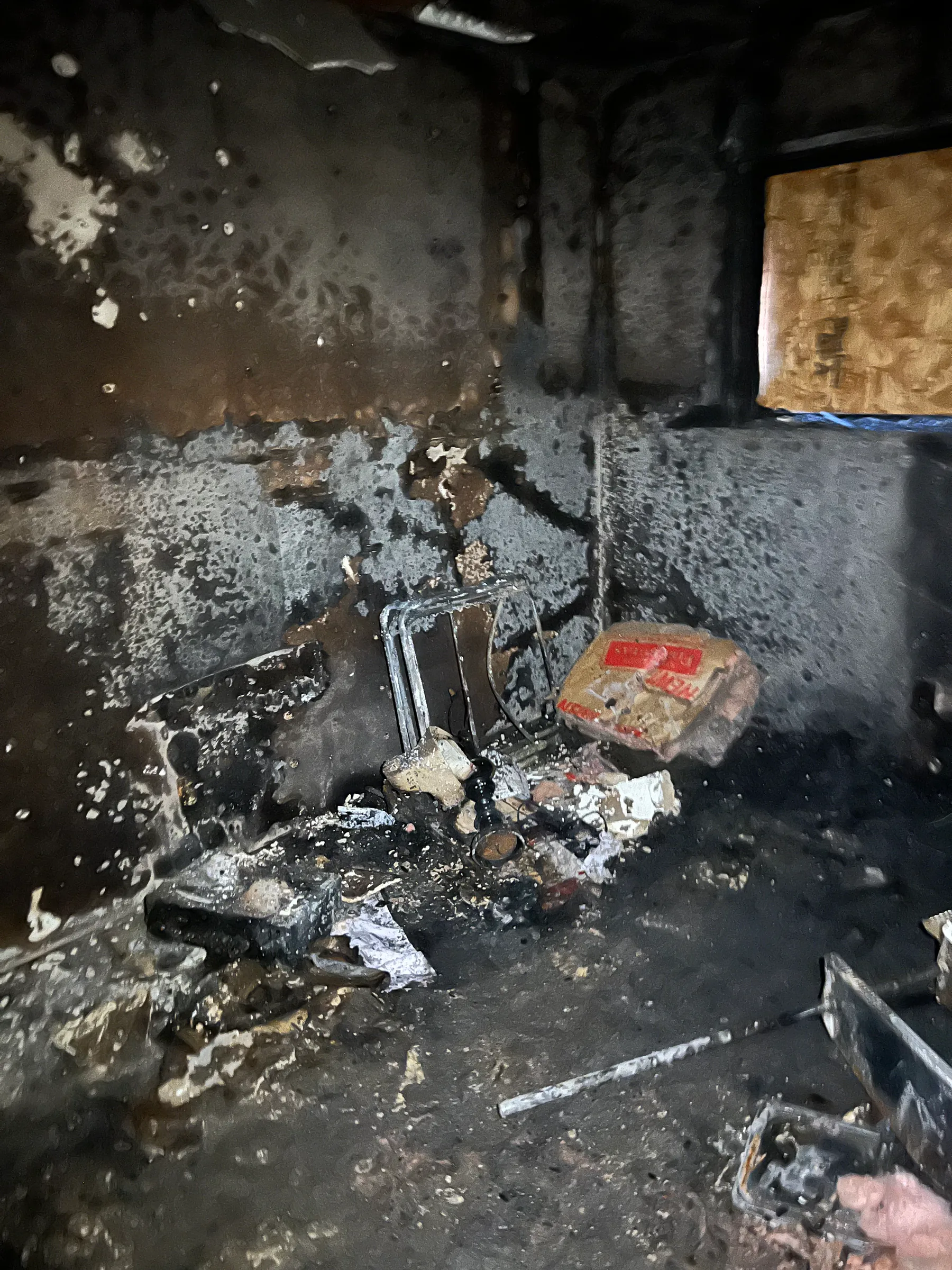 Charred room with soot-covered walls and damaged contents after a house fire