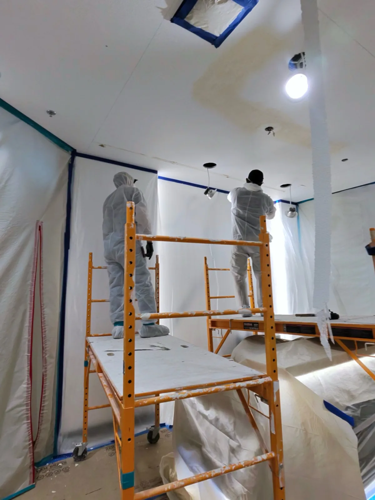 Quality 1st Restoration IICRC-certified crew in protective PPE working on scaffolding inside a fully contained workspace with plastic sheeting during a water damage ceiling restoration job in Henderson, NV