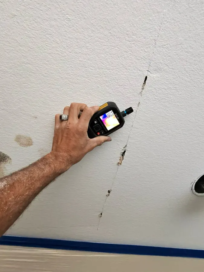 Technician scanning a cracked, water-stained upstairs ceiling with a thermal imaging moisture meter in The Lakes, Las Vegas