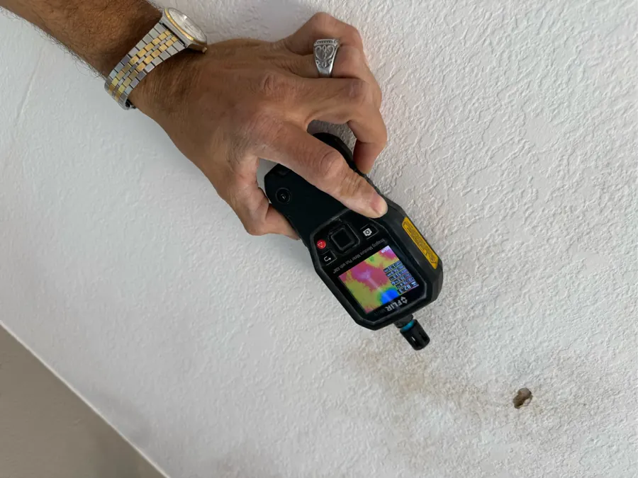 Thermal imaging moisture meter held against a stained downstairs ceiling below a balcony