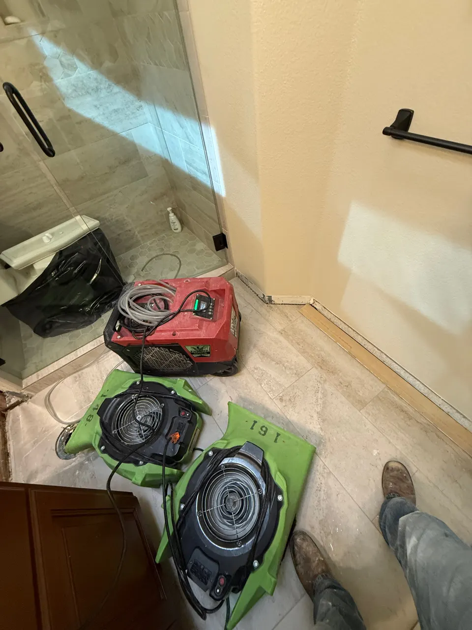 Air movers and a dehumidifier drying the wall beside a shower enclosure