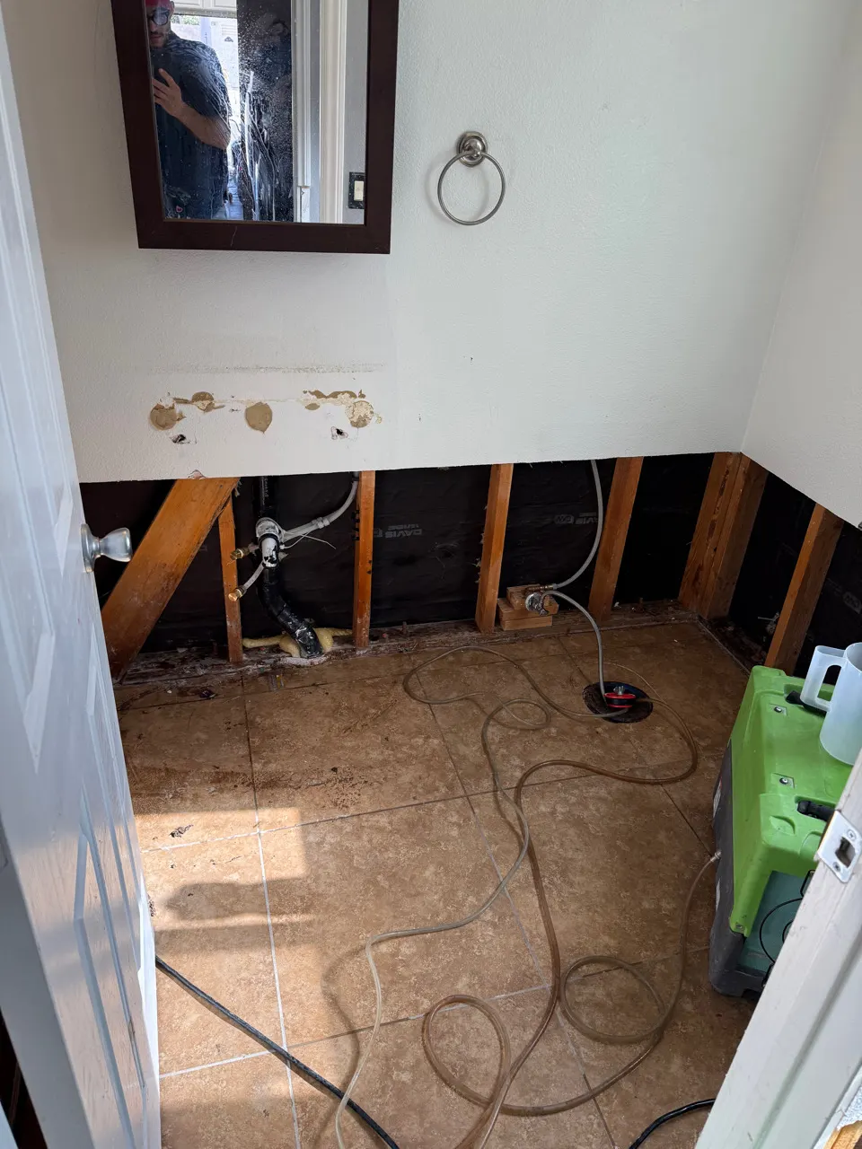Bathroom wall opened for drying with lower drywall removed and framing exposed during water damage cleanup