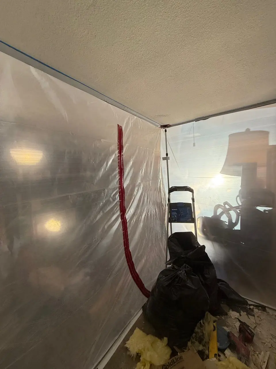Sealed plastic containment barrier and bagged debris inside a room during mold removal